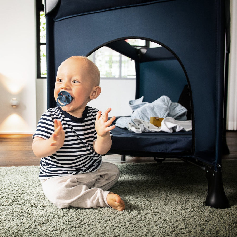Baby playing in front of a Hauck travel cot with the side zip door open